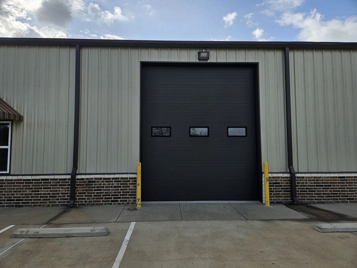 Black commercial sectional door with windows on a steel building
